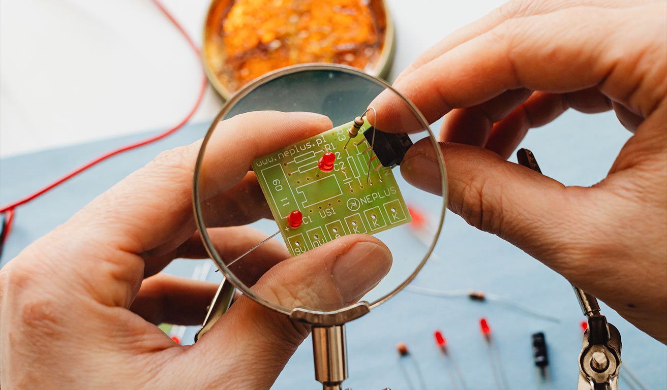 Foto: Ein Computerchip mit zwei Händen unter einer Lupe