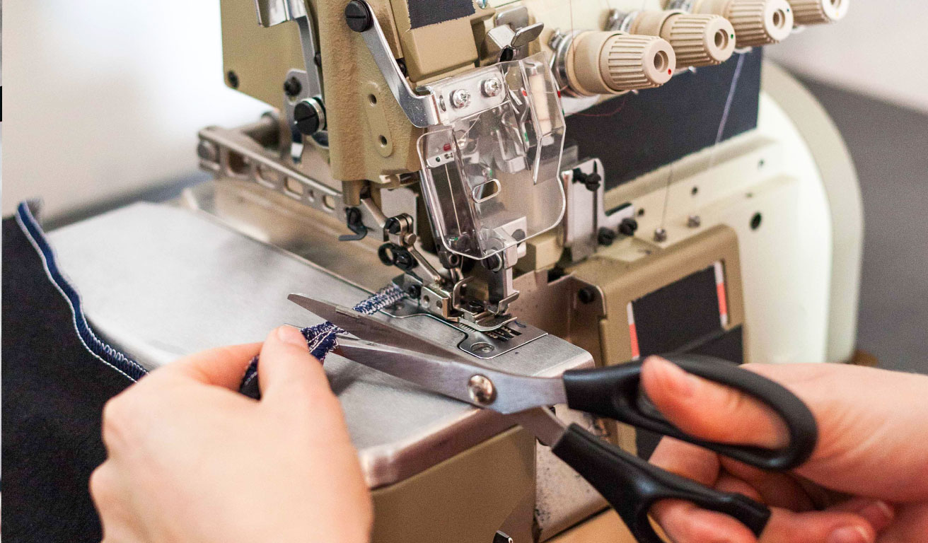 Foto: Eine Nähmaschine und Hände mit einer Schere