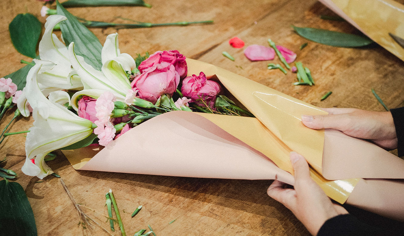 Foto: Hände wickeln ein Bouquet aus Rosen und Lilien in Papier ein.