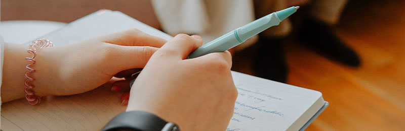 Foto: Eine Person hält einen Stift über einem Notizbuch.