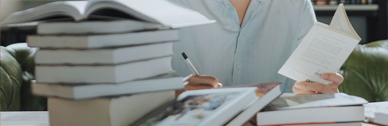 Foto: Mehrere Bücher und eine Frau, die schreibt.