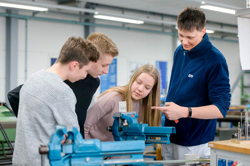 Foto: Ein Mann zeigt drei Jungen eine Maschine.