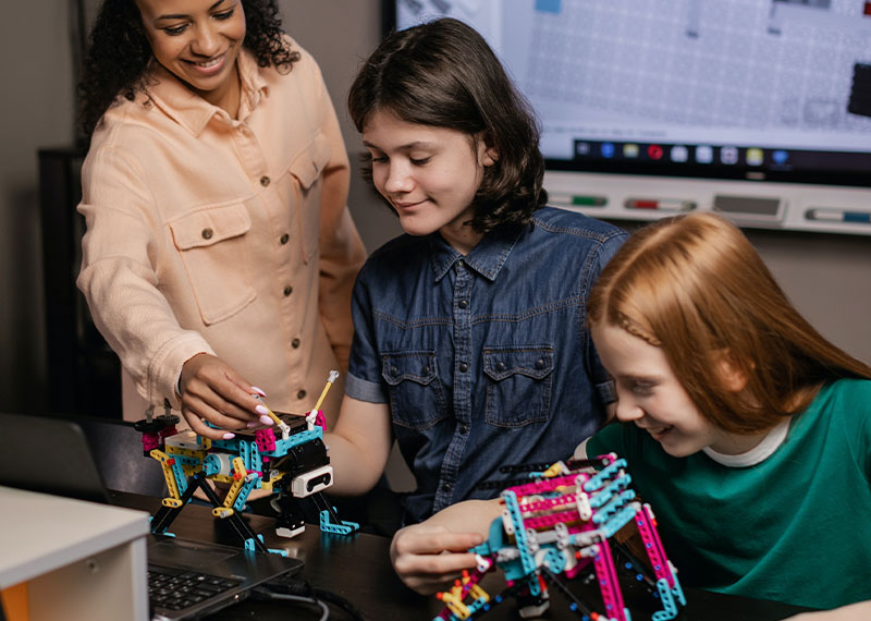 Foto: Eine Frau und zwei Mädschen arbeiten mit einem bunten Robotermodell.