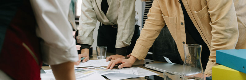 Foto: Mehrere Personen mit Händen auf Tisch mit Papieren