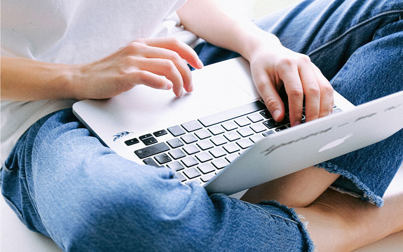 Foto: Eine Person tippt auf einem Laptop, der auf dem Schoß liegt.