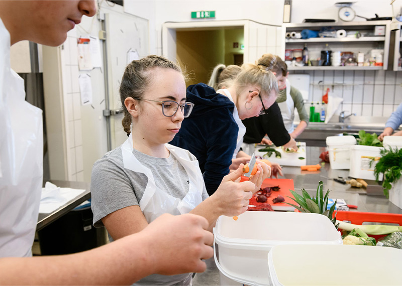 Foto: Personen arbeiten in einer Küche und bereiten Essen vor.