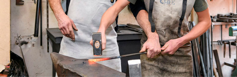 Foto: Zwei Personen hämmern auf eine glühende Metallstange.
