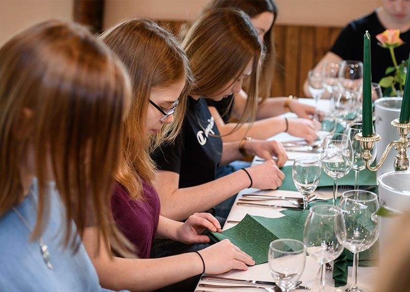 Foto: Jugendliche falten Servietten an einem Tisch mit Geschirr.