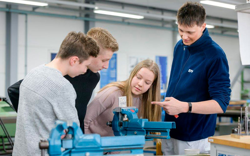 Foto: Ein Mann zeigt drei Jungen eine Maschine.