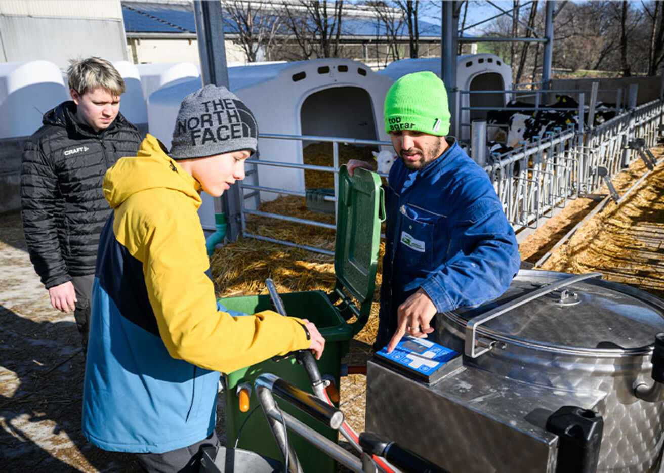 Foto: Drei Personen arbeiten mit landwirtschaftlichen Geräten im Freien.
