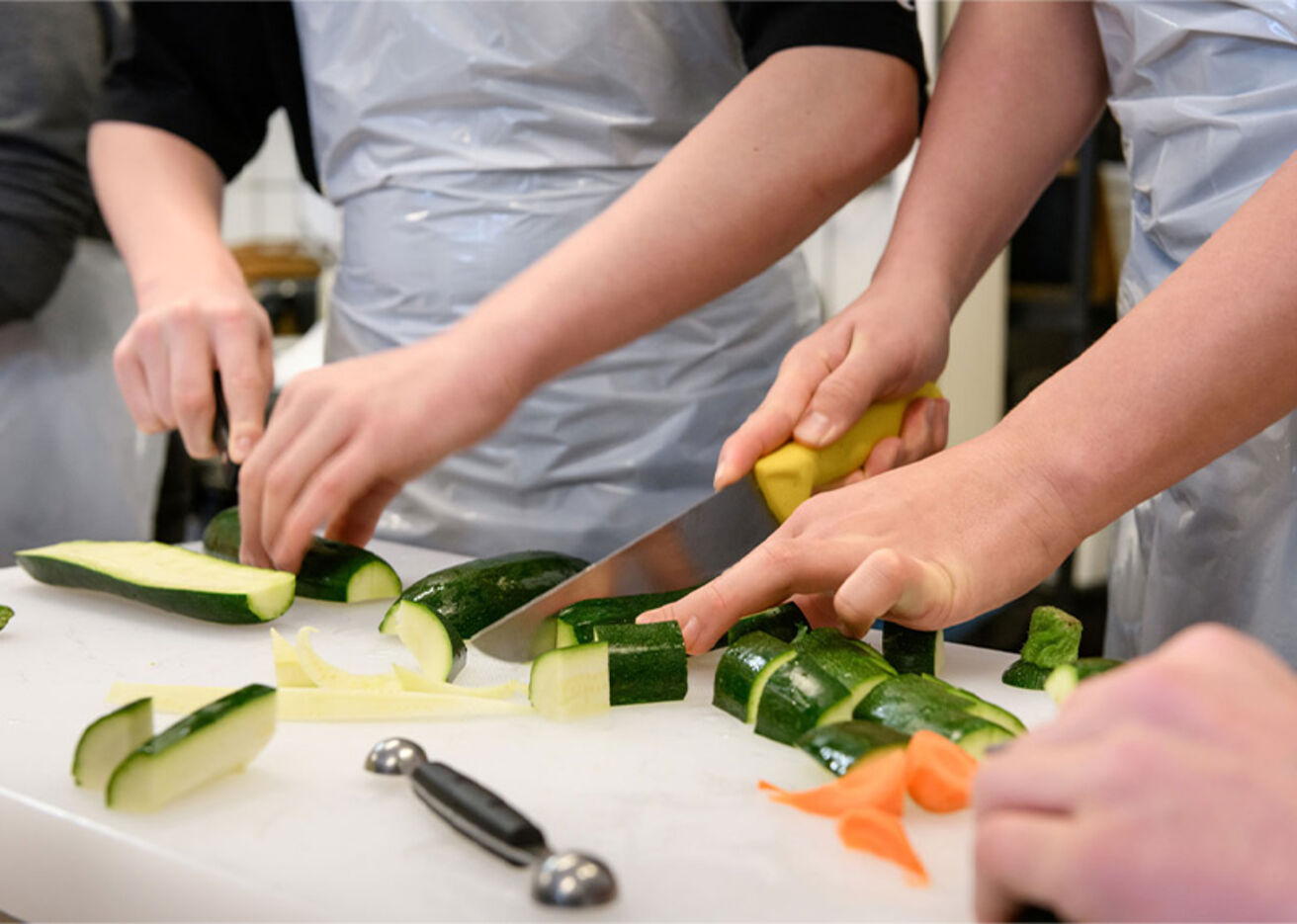 Foto: Hände schneiden Zucchini auf einem Schneidebrett.