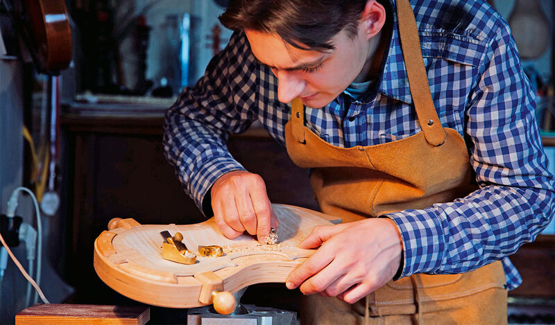 Foto: Ein Handwerker bearbeitet das Holz einer Violine.
