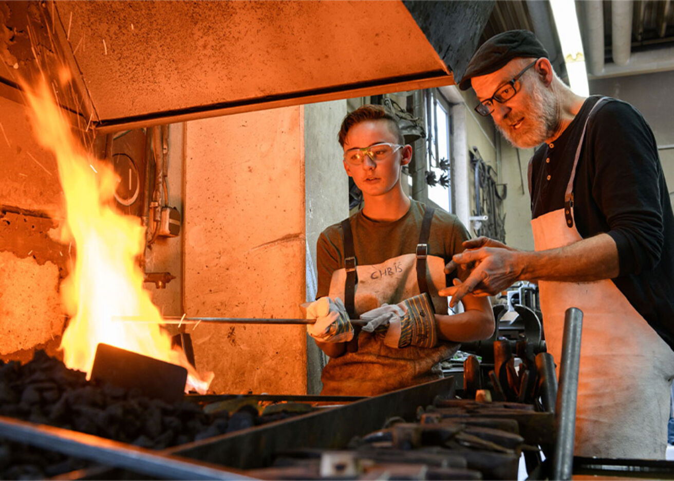 Foto: Ein Arbeiter zeigt einem Jungen, wie man über dem Feuer schmiedet.