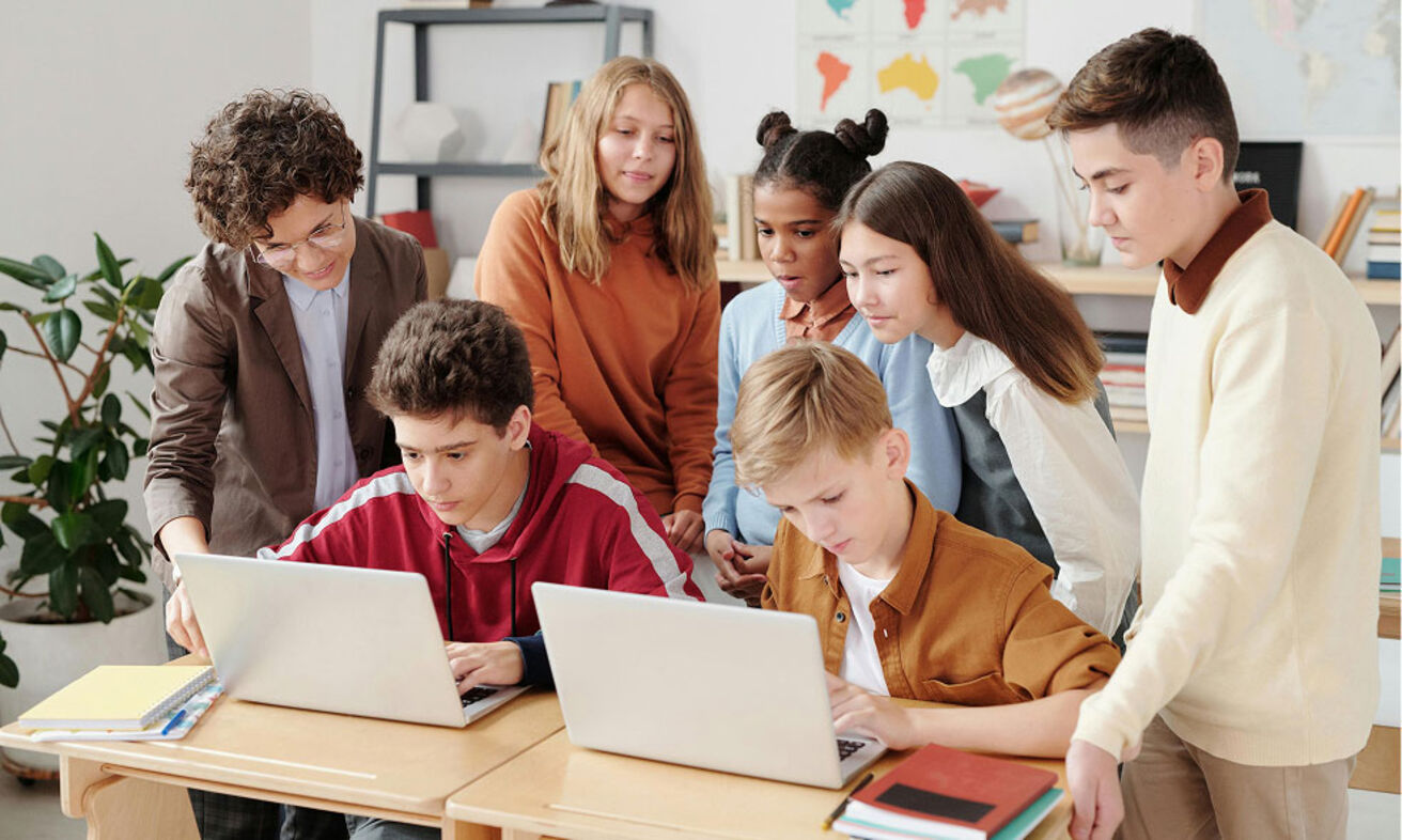 Foto: Einer Lehrerin zeigt Jugendlichen etwas am Rechner.