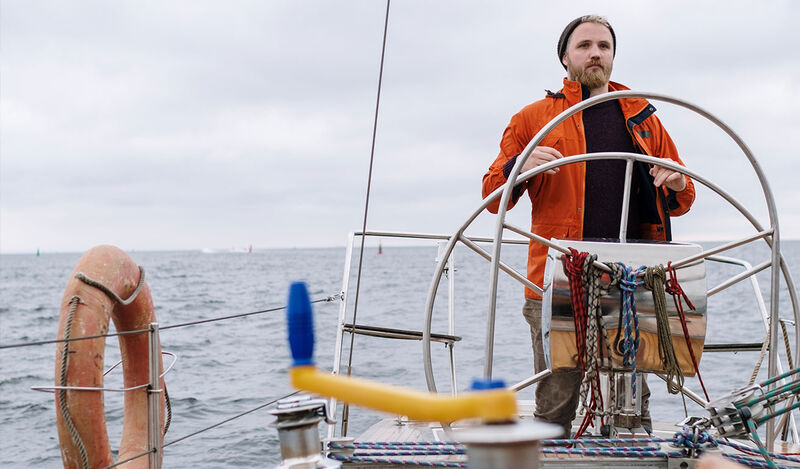 Foto: Ein Mann steht am Steuer eines Segelbootes auf dem offenen Meer.