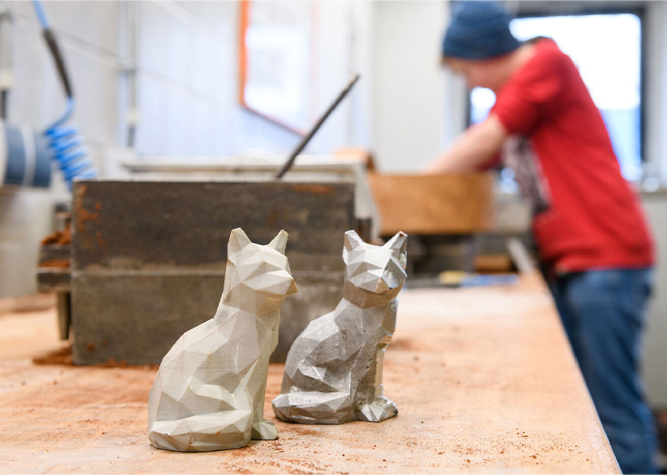 Foto: Zwei Skulpturen stehen auf einem Tisch, eine Person befindet sich im Hintergrund.