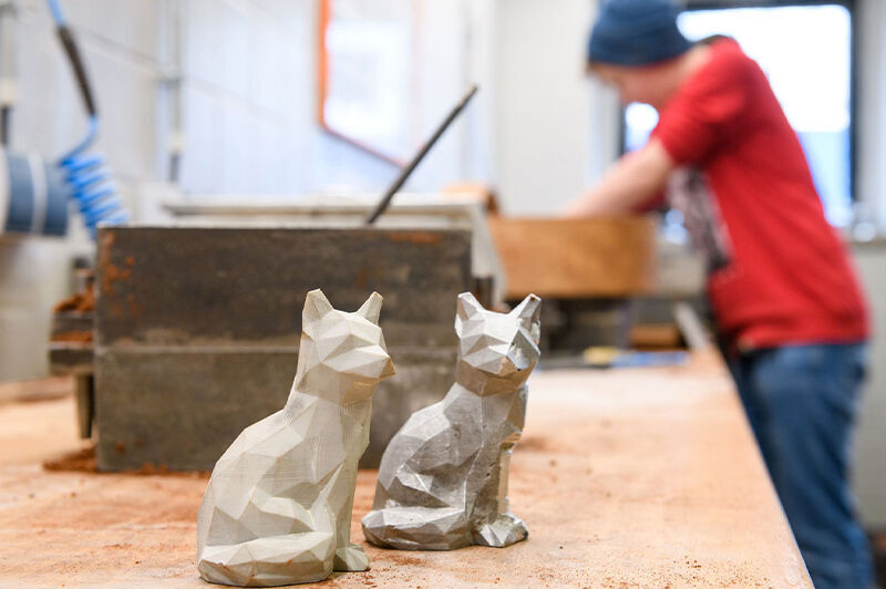 Foto: Zwei Skulpturen stehen auf einem Tisch, eine Person befindet sich im Hintergrund.