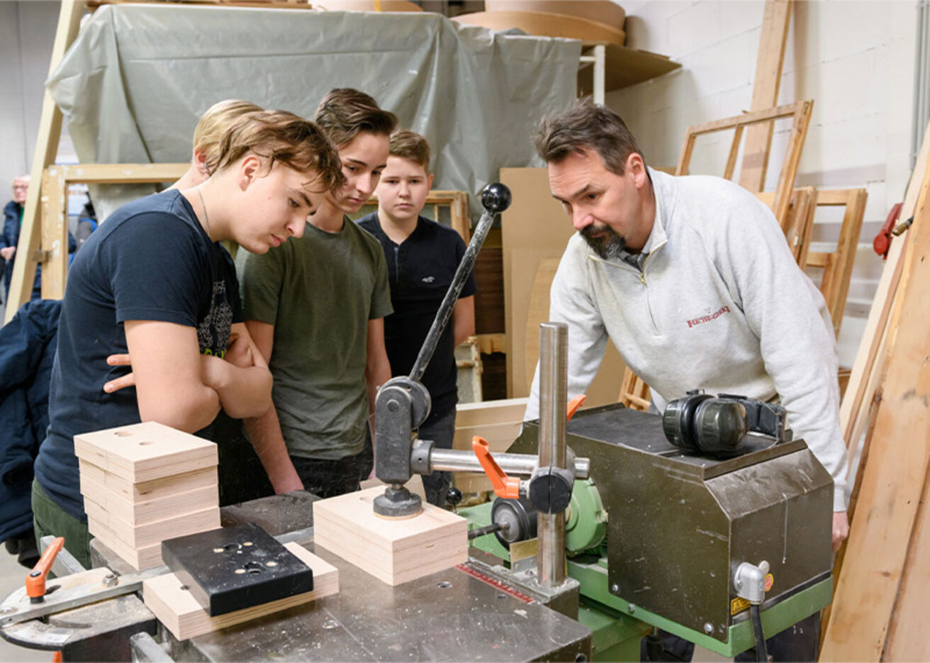 Foto: Ein Mann und vier Jungen beobachten ein Holzprojekt in einer Werkstatt.